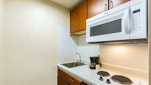 A compact kitchen with a built-in microwave, a sink, and a stovetop. - HomeTowne Studios by Red Roof Atlanta - Norcross Downtown (Norcross)