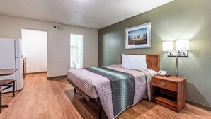 A hotel room with a bed, bedside table, lamp, and a painting on the wall.