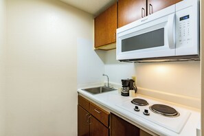 Una kitchenette compacta con microondas, cafetera y estufa.