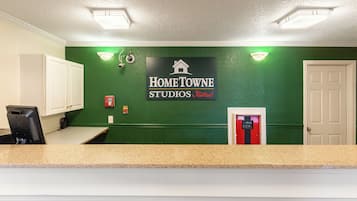 A reception area with a green wall, a sign for Home Towne Studios by RedRoof, a fire extinguisher, and a door.