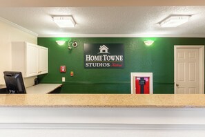 A reception area with a green wall, a sign for Home Towne Studios by RedRoof, a fire extinguisher, and a door. - HomeTowne Studios by Red Roof Atlanta - Norcross Downtown (Norcross)