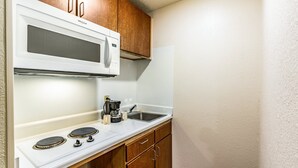 A compact kitchen with a white microwave, stove, and sink. - HomeTowne Studios by Red Roof Atlanta - Norcross Downtown (Norcross)