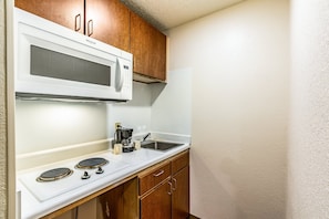 Cocina compacta con microondas, estufa y lavamanos blancos.