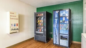 Two vending machines, one with a coin slot and the other with a card payment system, against a green wall with a whiteboard above.