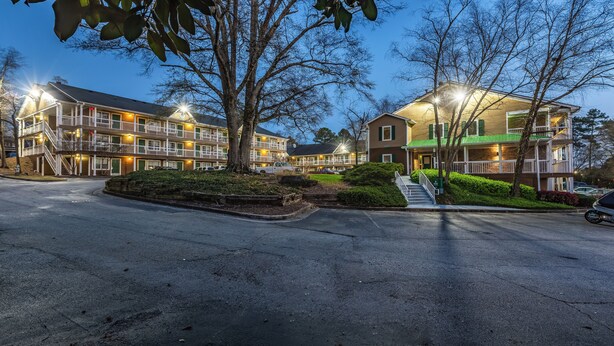 A multi-story hotel with balconies, a parking lot, and a well-maintained lawn.