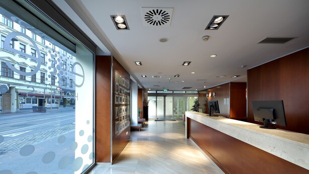 Un moderno hall de hotel con un mostrador de recepción, un amplio ventanal con vista a la calle y una pared de vidrio con diseño.