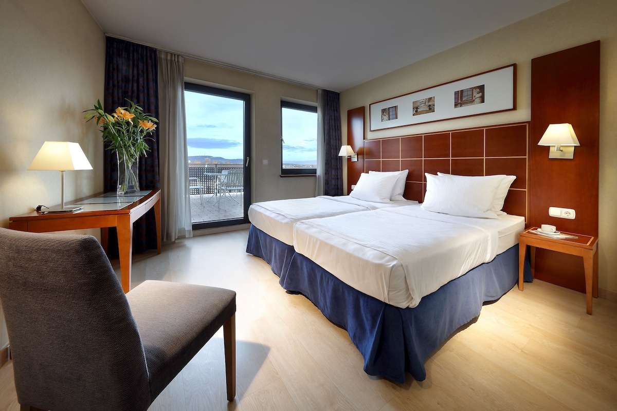 A hotel room with a bed, a desk, a chair, and a view of the outdoors.