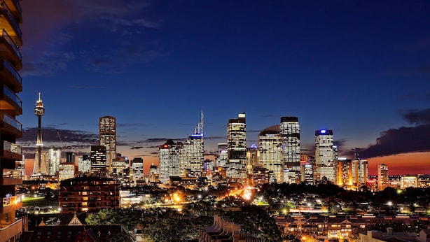 Une vue nocturne sur les gratte-ciel d’une ville, avec des bâtiments illuminés et une tour imposante.