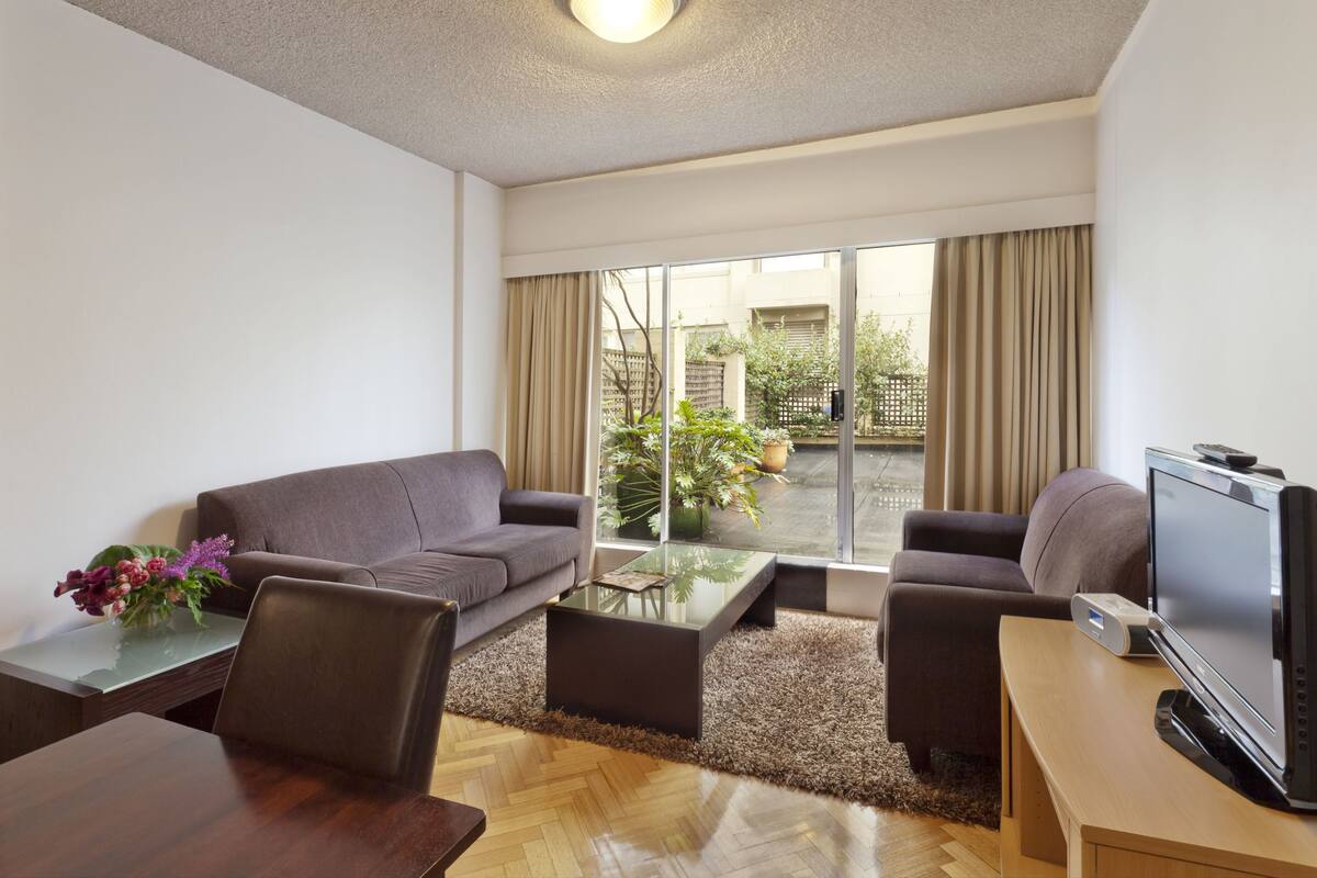 Una sala de estar moderna con un sofá, una mesa de centro, televisor y vistas al exterior.