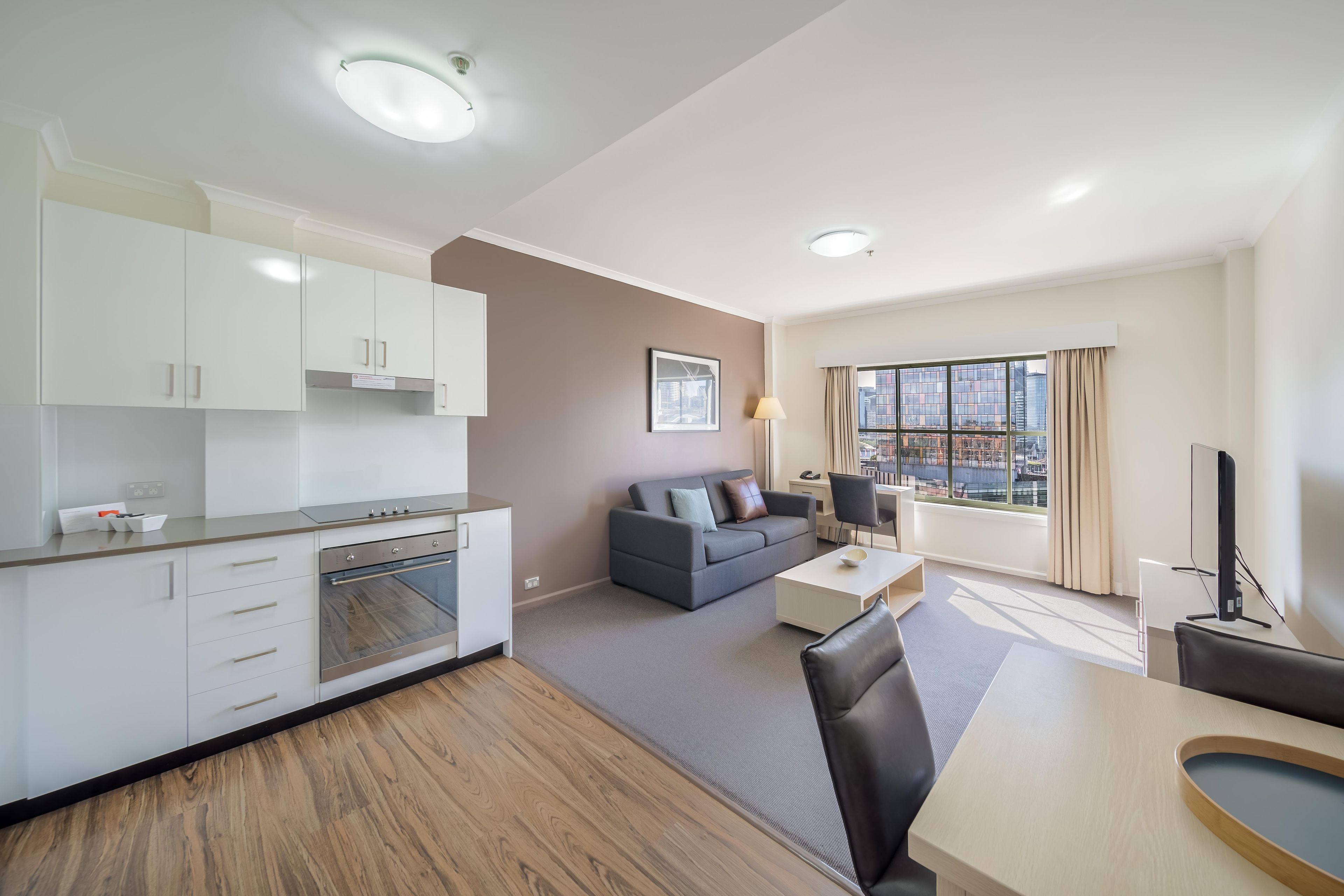 Un apartamento moderno con kitchenette, sala de estar con sofá y mesa de comedor, y un ventanal con vistas a la ciudad.