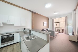 A modern kitchen with a built-in oven, a stainless steel sink, and a dining area with a table and chairs. - Oaks Sydney Goldsbrough Suites (Pyrmont)