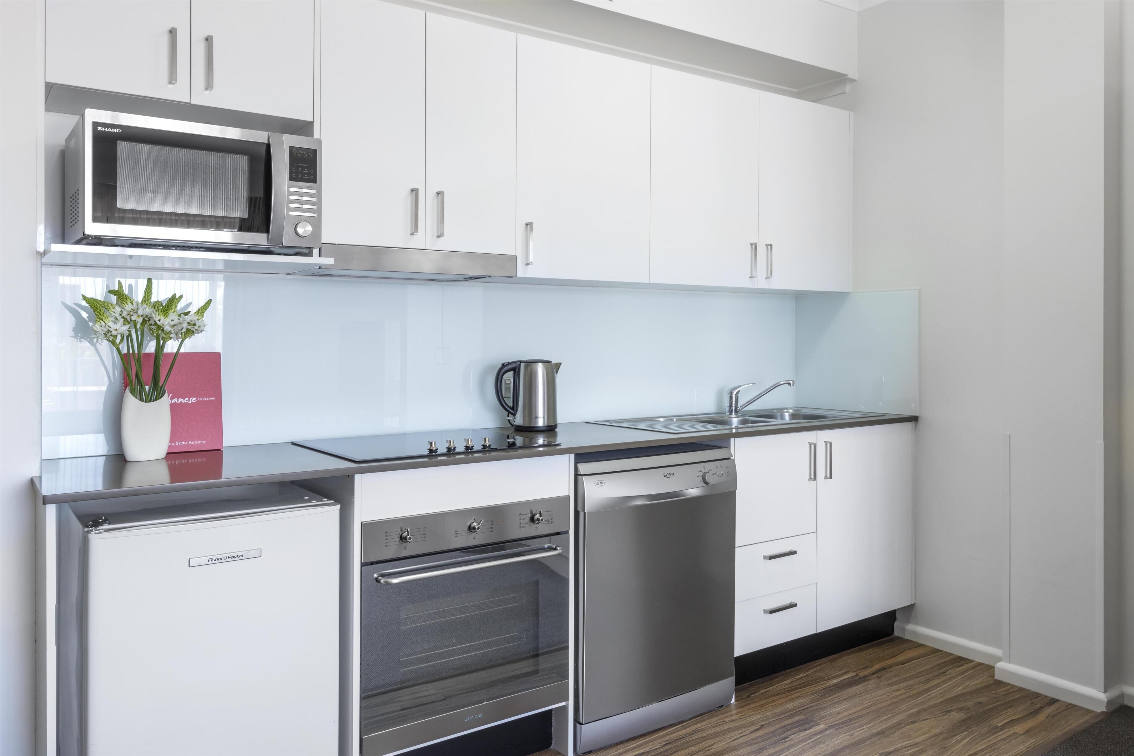 A modern kitchen with stainless steel appliances, white cabinetry, and a wooden floor.