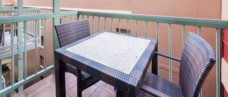 A balcony with a table and two chairs, a brick wall, and a metal railing.