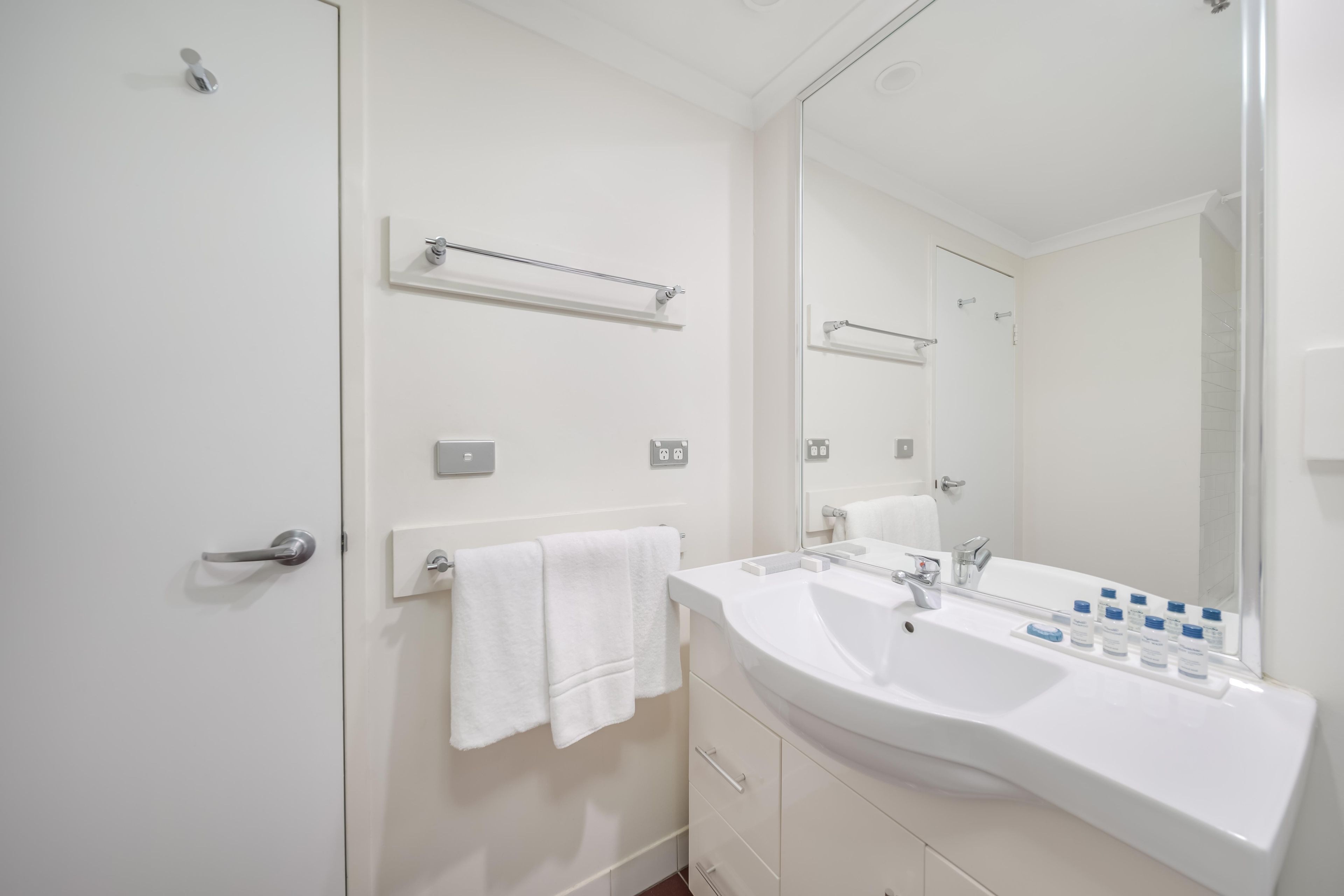 A modern bathroom with a large mirror, two sinks, and a towel rack.