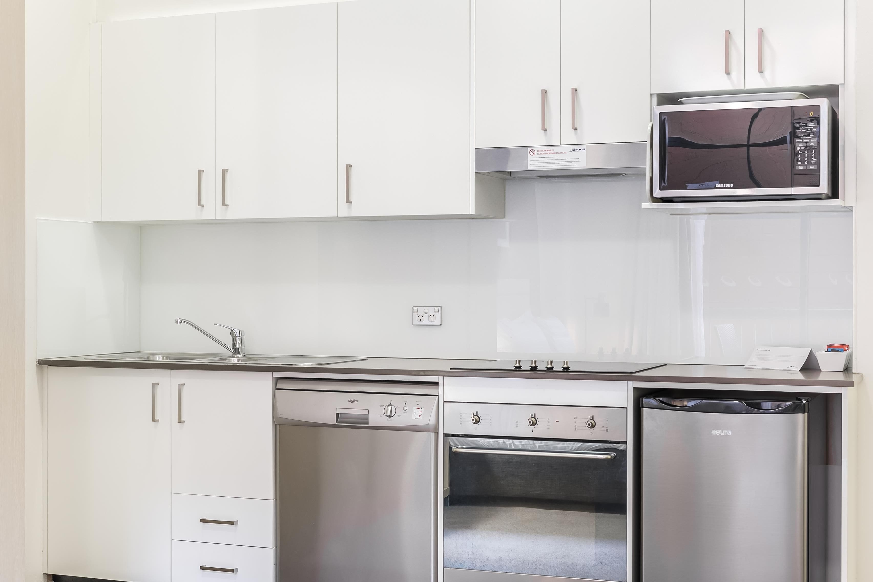Une cuisine moderne avec des meubles blancs, un four à micro-ondes encastré, un lave-vaisselle et un four.