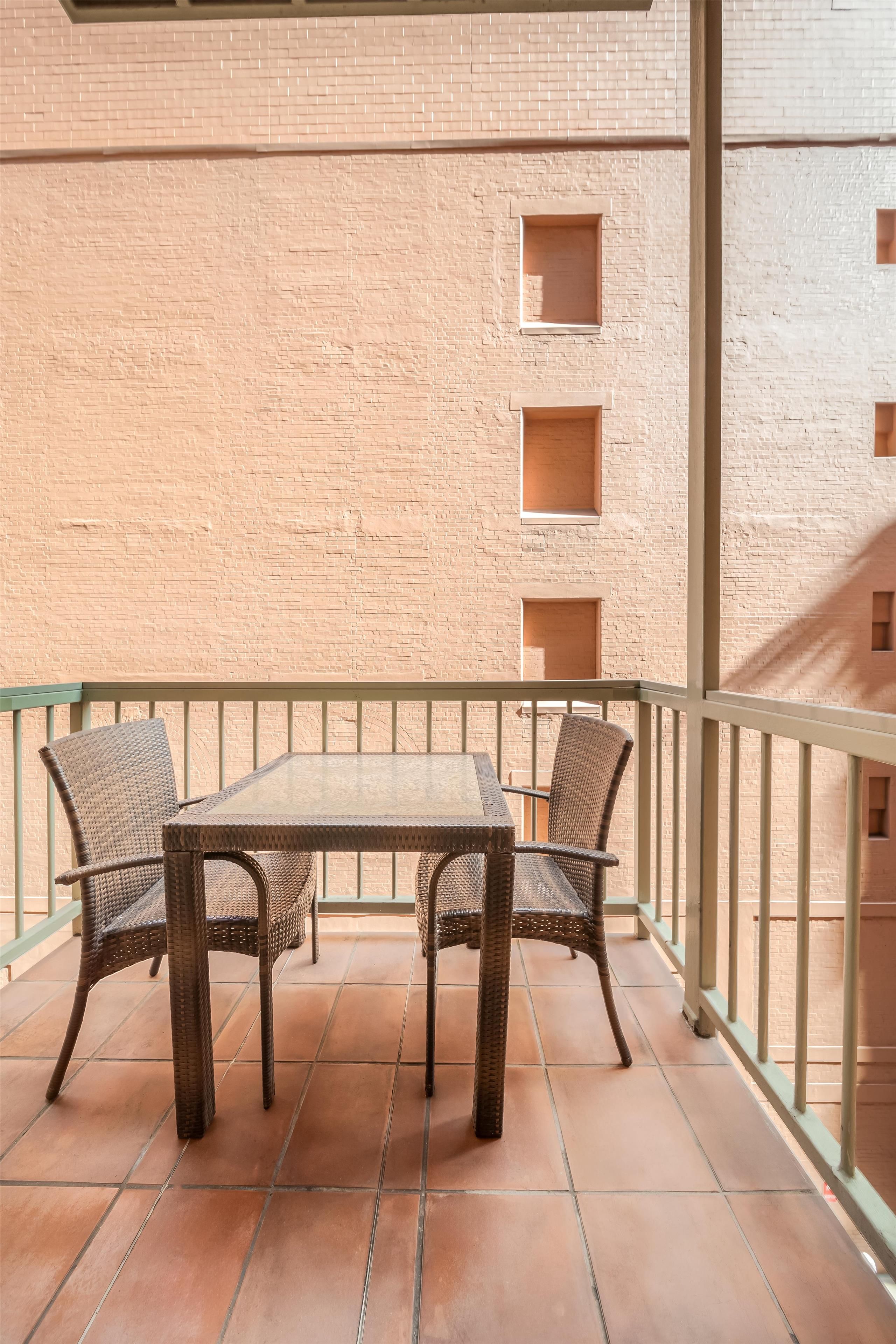 A balcony with a table and chairs, a tiled floor, and a brick wall.