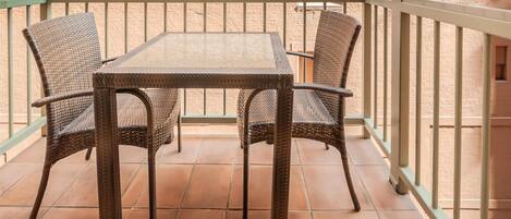 A balcony with a table and chairs, a tiled floor, and a brick wall.