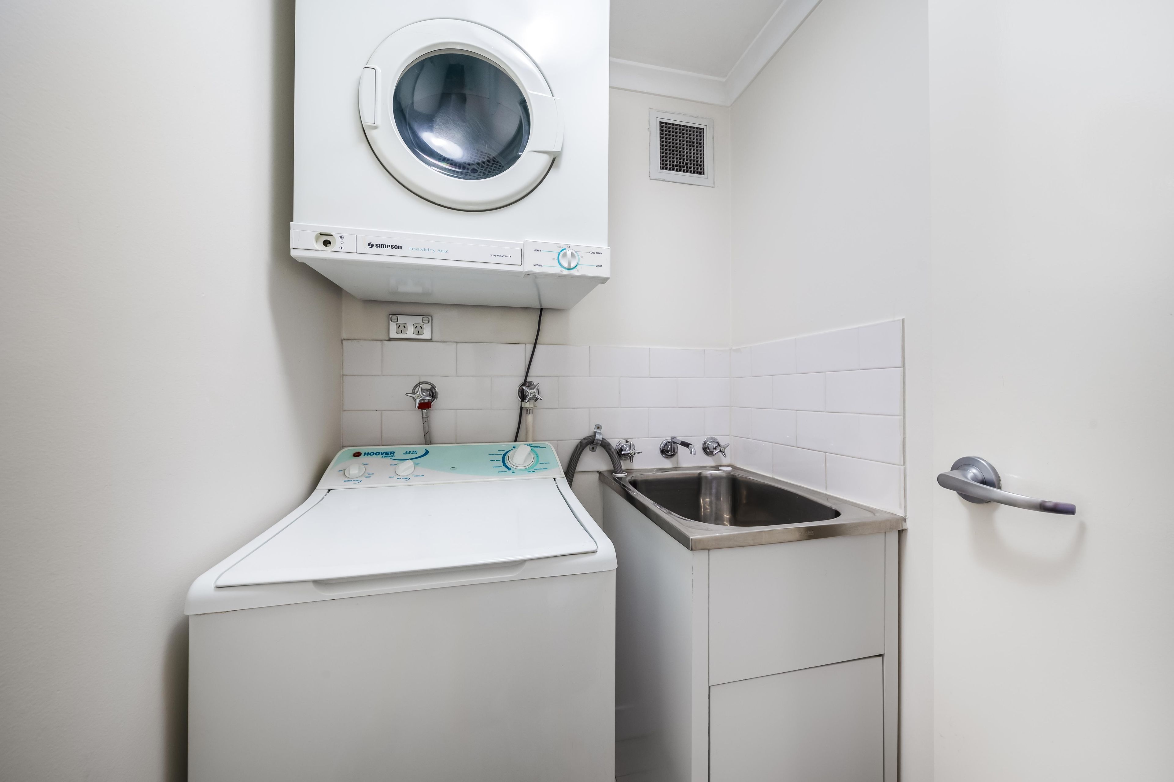 A laundry area with a front-loading washing machine, a sink, and a towel rack.