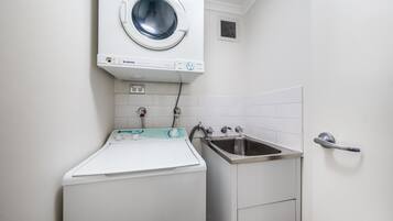 A laundry area with a front-loading washing machine, a sink, and a towel rack.