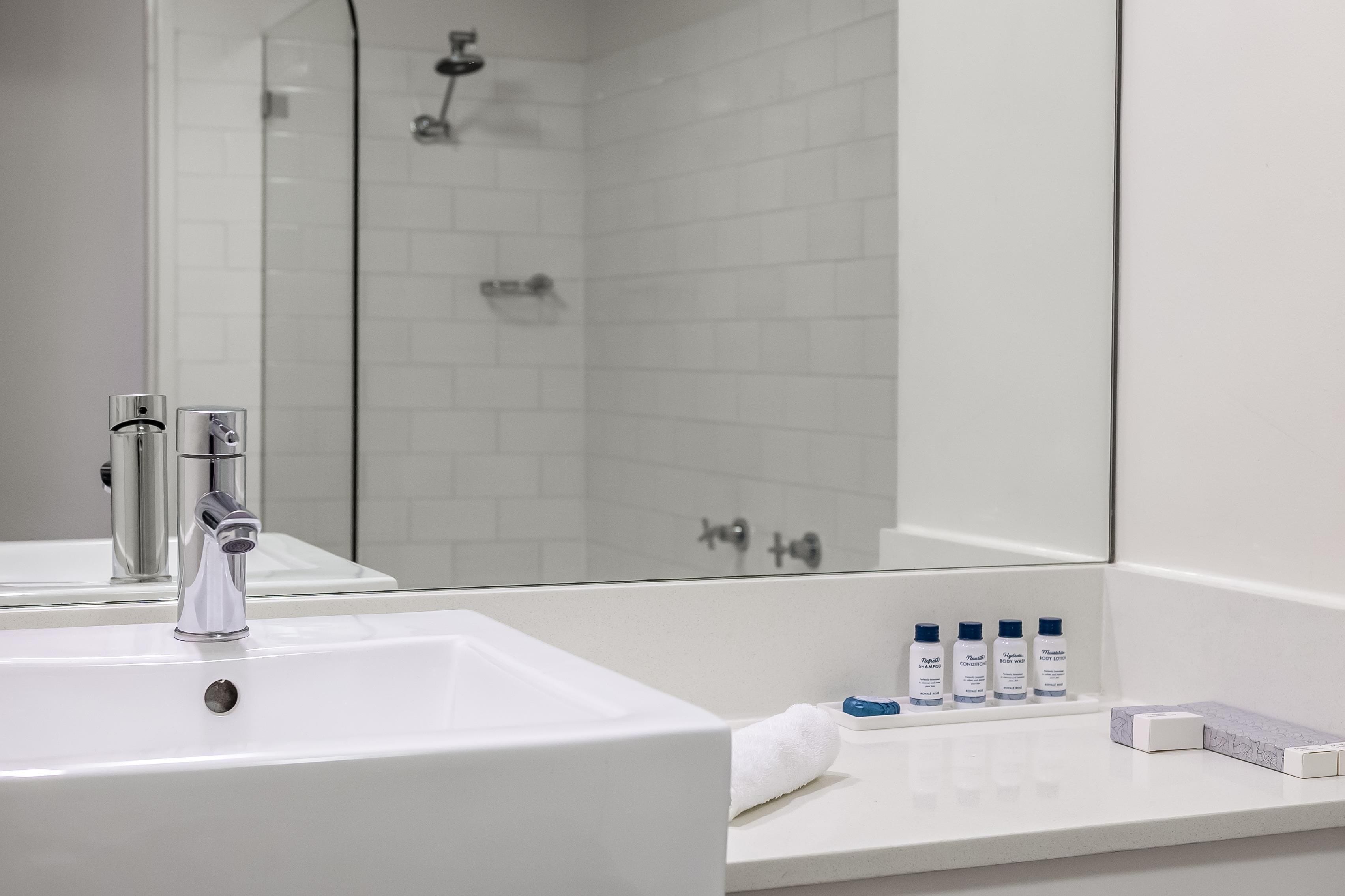 Un baño con lavamanos blanco, espejo y ducha.
