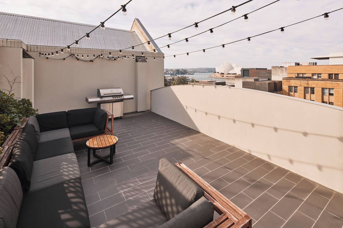 A rooftop terrace with a sectional sofa, a small round table, and string lights.