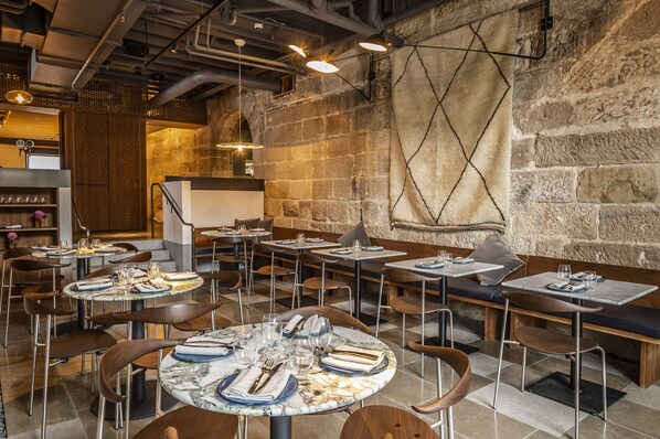 A restaurant with round tables set for dining, stone walls, and hanging lights.