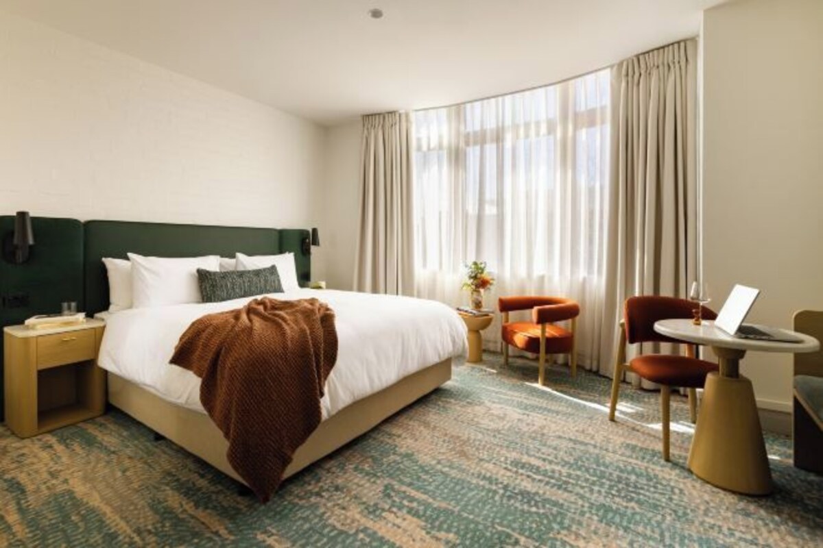 Habitación de hotel con cama, escritorio, silla y ventana con cortinas.