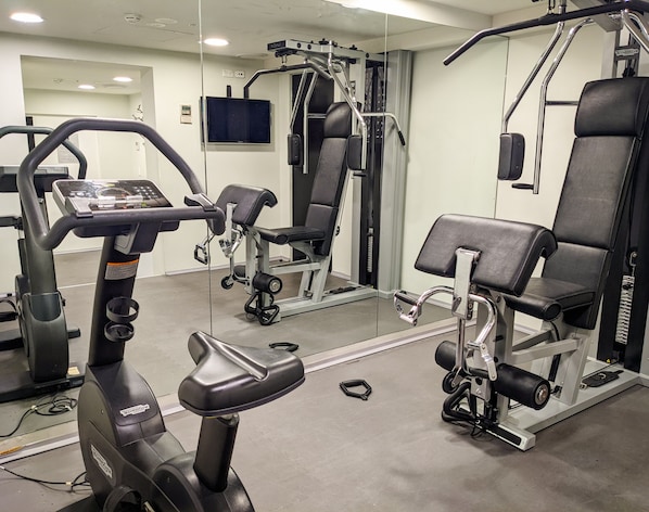 A gym with exercise equipment, mirrors, and a treadmill.