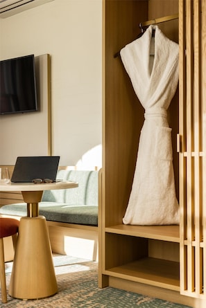 A hotel room with a wooden wardrobe, a flat-screen TV mounted on the wall, a laptop on a small table, and a bed with a green and white patterned bedspread.