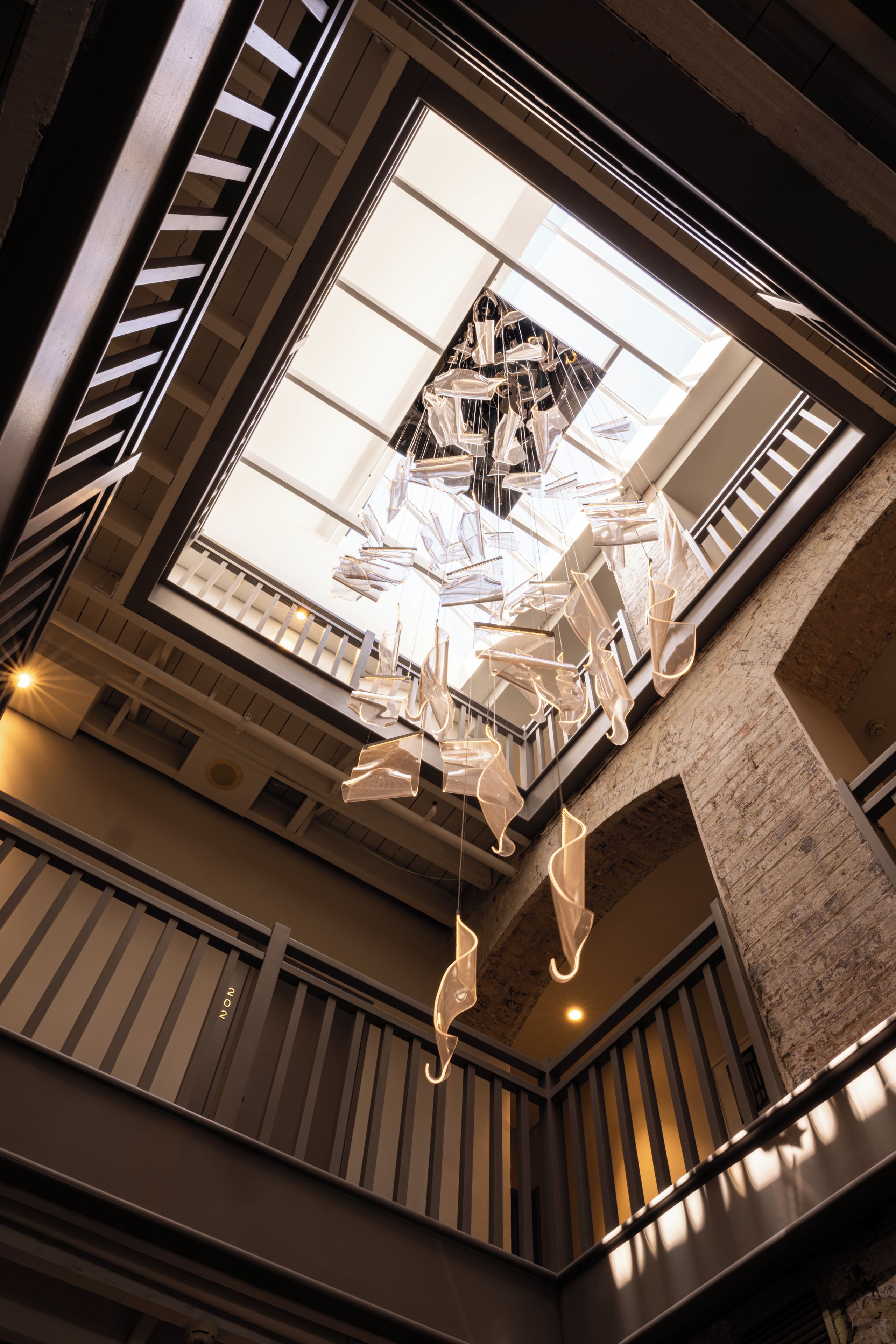 A modern interior with a unique ceiling sculpture, a staircase, and a view of the sky through a skylight.