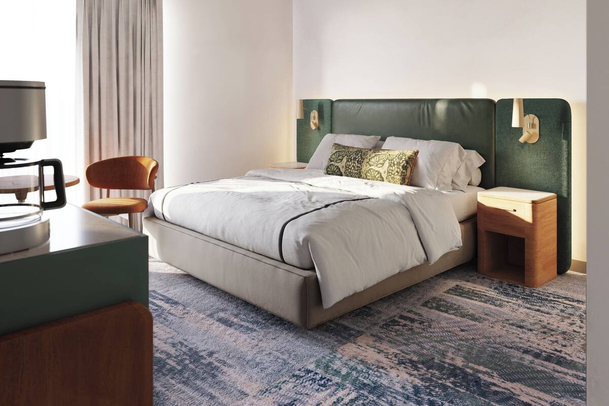 A modern hotel room with a large bed, a desk, a chair, and a television.
