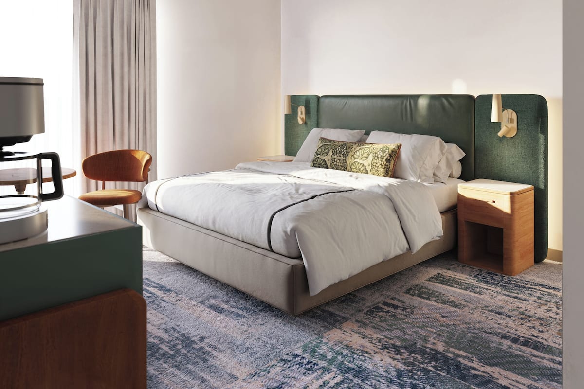 A modern hotel room with a large bed, a desk, a chair, and a television.