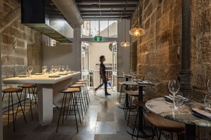 A restaurant with a stone wall interior, a central bar area, and a person walking through the entrance.