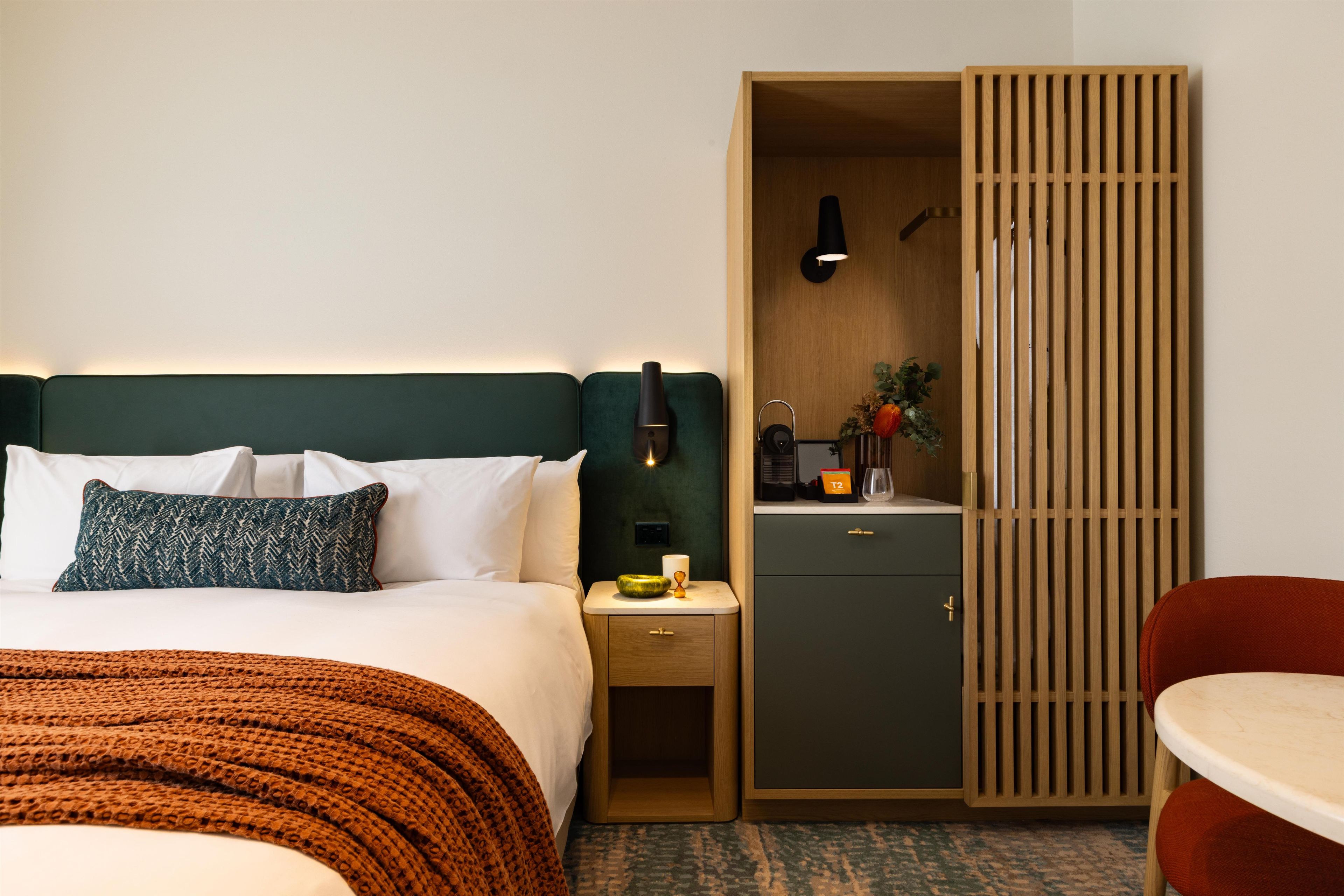 Habitación de hotel con cama, mesita de noche, armario y una pequeña mesa con una silla.
