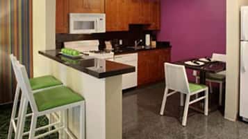 Cozinha compacta com ilha central, dois bancos de bar, micro-ondas e geladeira.