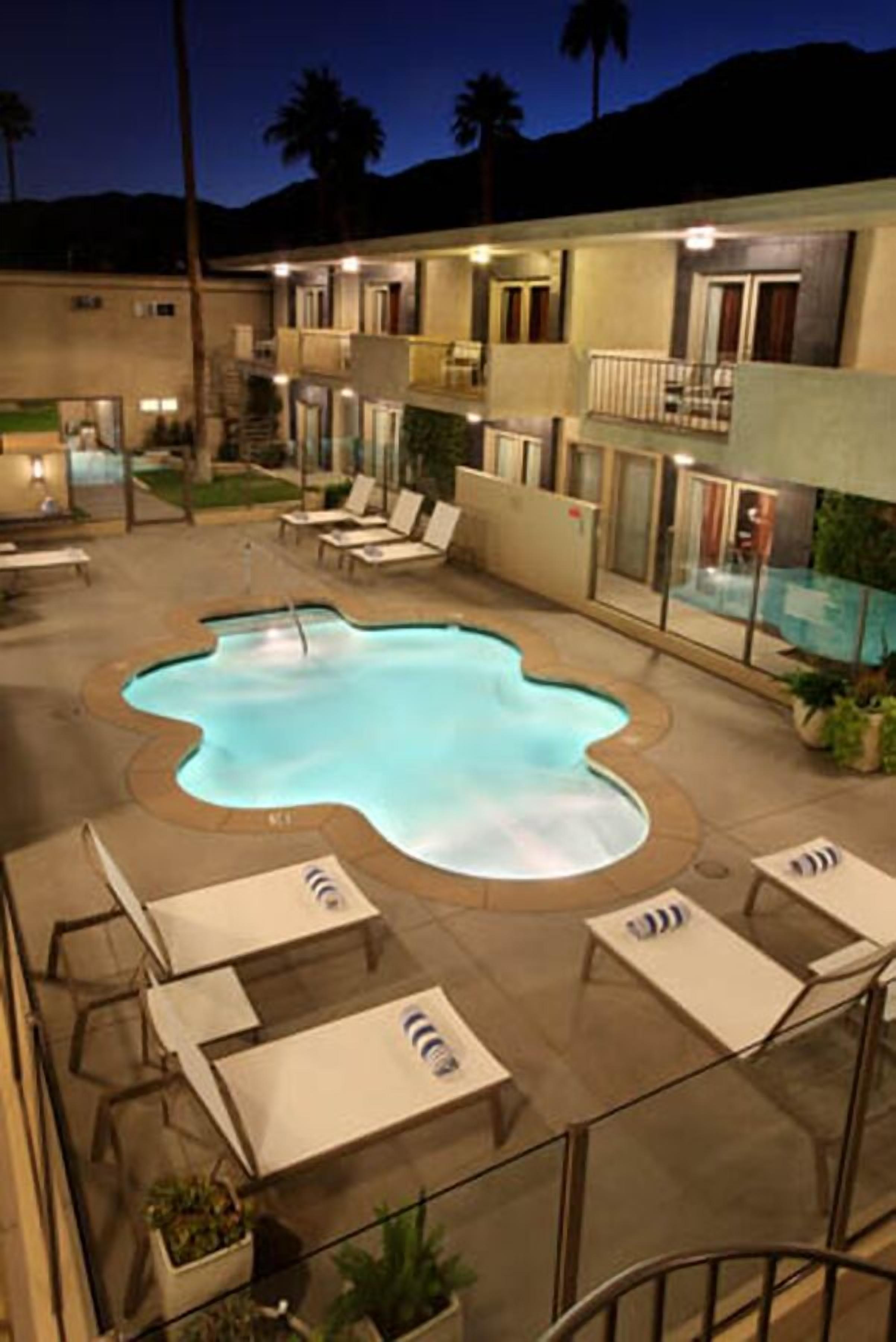 Un hotel con piscina, sillones de descanso y una escalera que lleva a los pisos superiores.