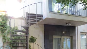 Un edificio moderno con una escalera que conduce a un balcón, una puerta con la etiqueta “130” y asientos al aire libre.