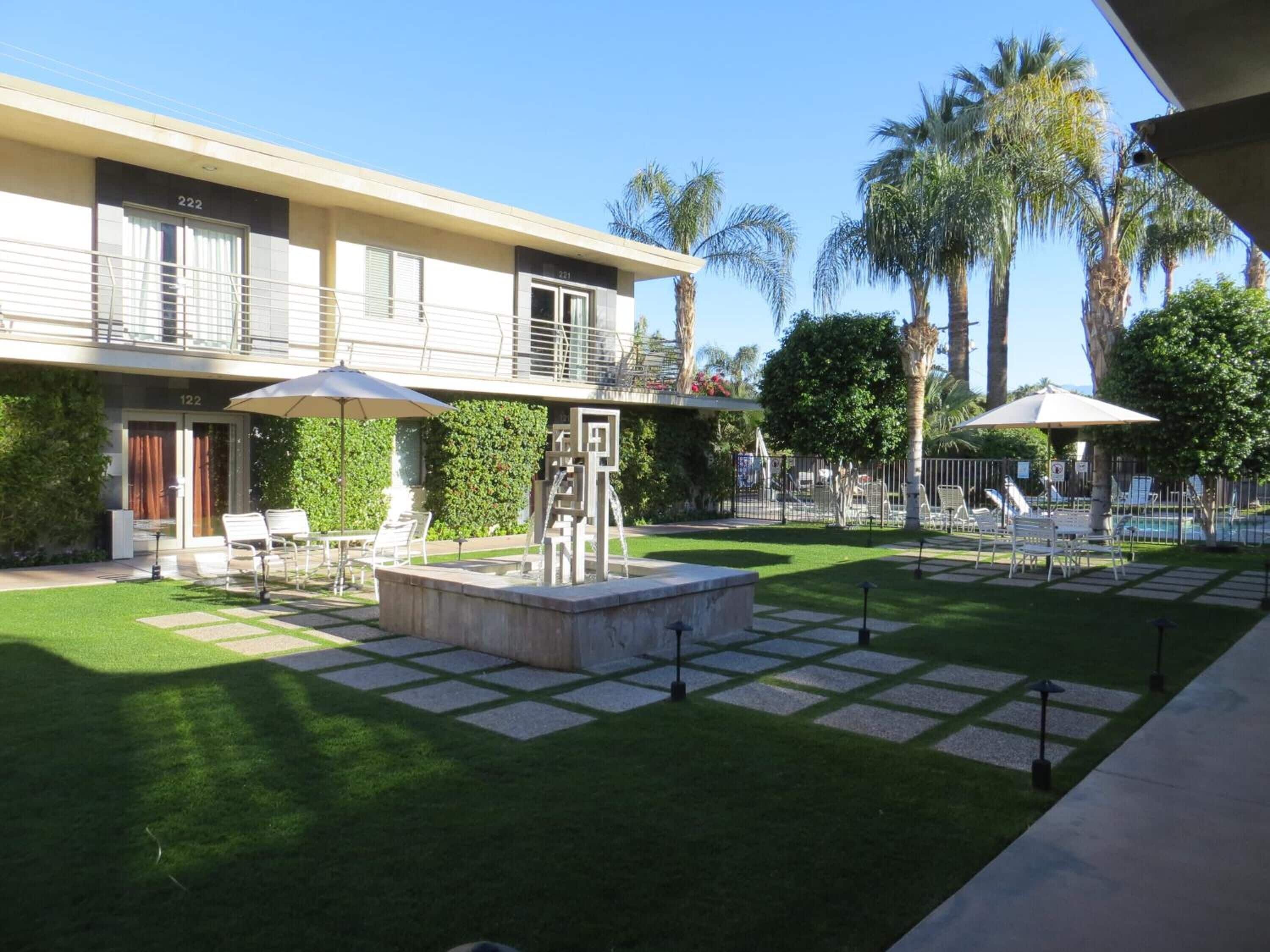 A hotel with a pool area, outdoor seating, and palm trees.
