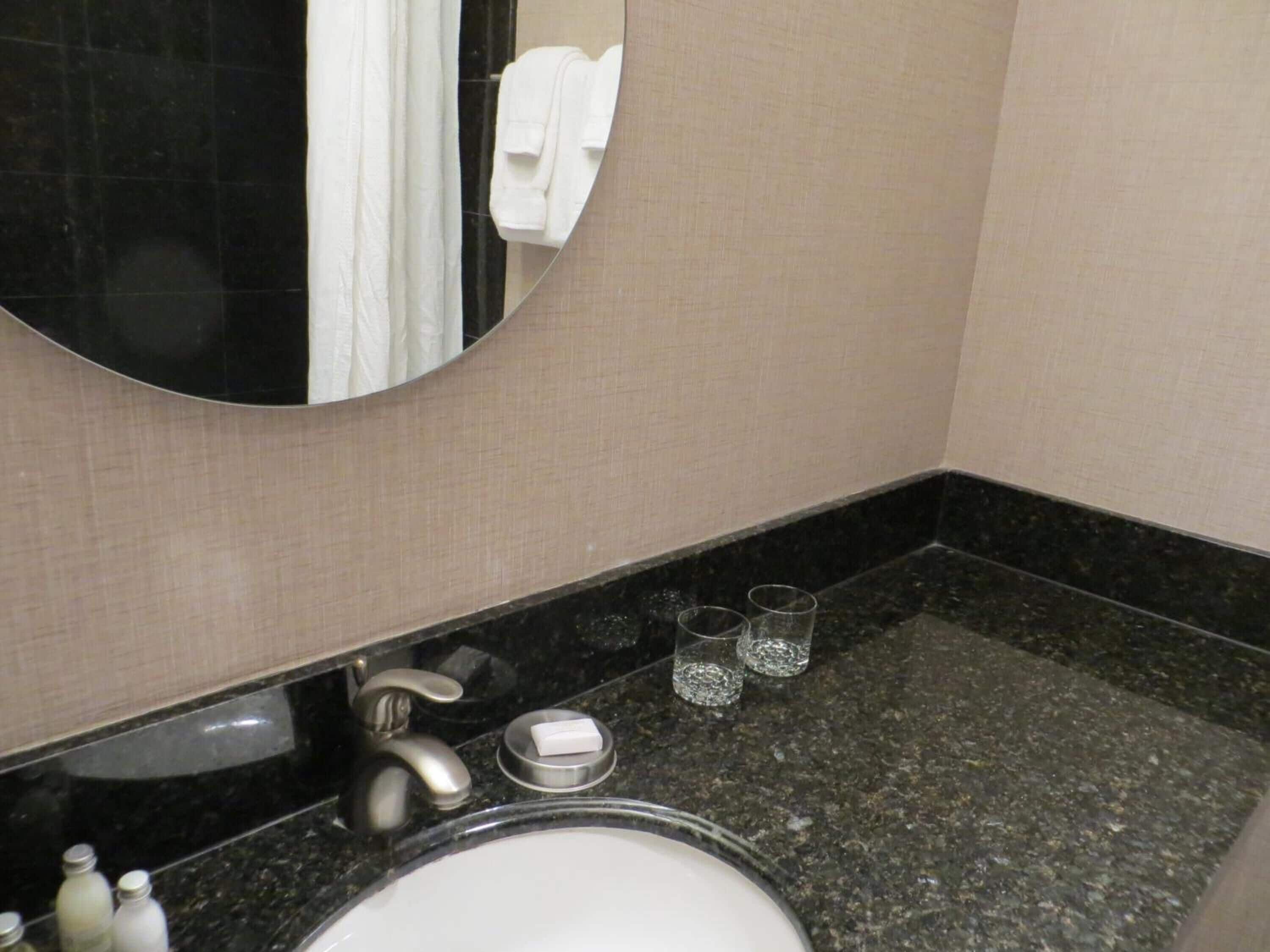 Un baño con un espejo redondo, un lavabo, un grifo y dos vasos sobre la encimera.