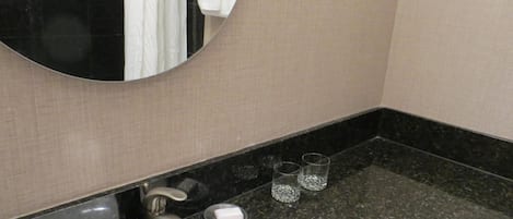 Un baño con un espejo redondo, un lavabo, un grifo y dos vasos sobre la encimera.