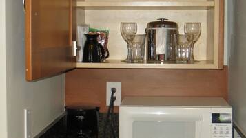 A kitchen with a microwave, coffee maker, and glassware on shelves.