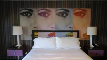 Een hotelkamer met een bed, twee nachtkastjes met lampen, een hoofdbord met een kleurrijk ontwerp, en een groot kunstwerk boven het bed.