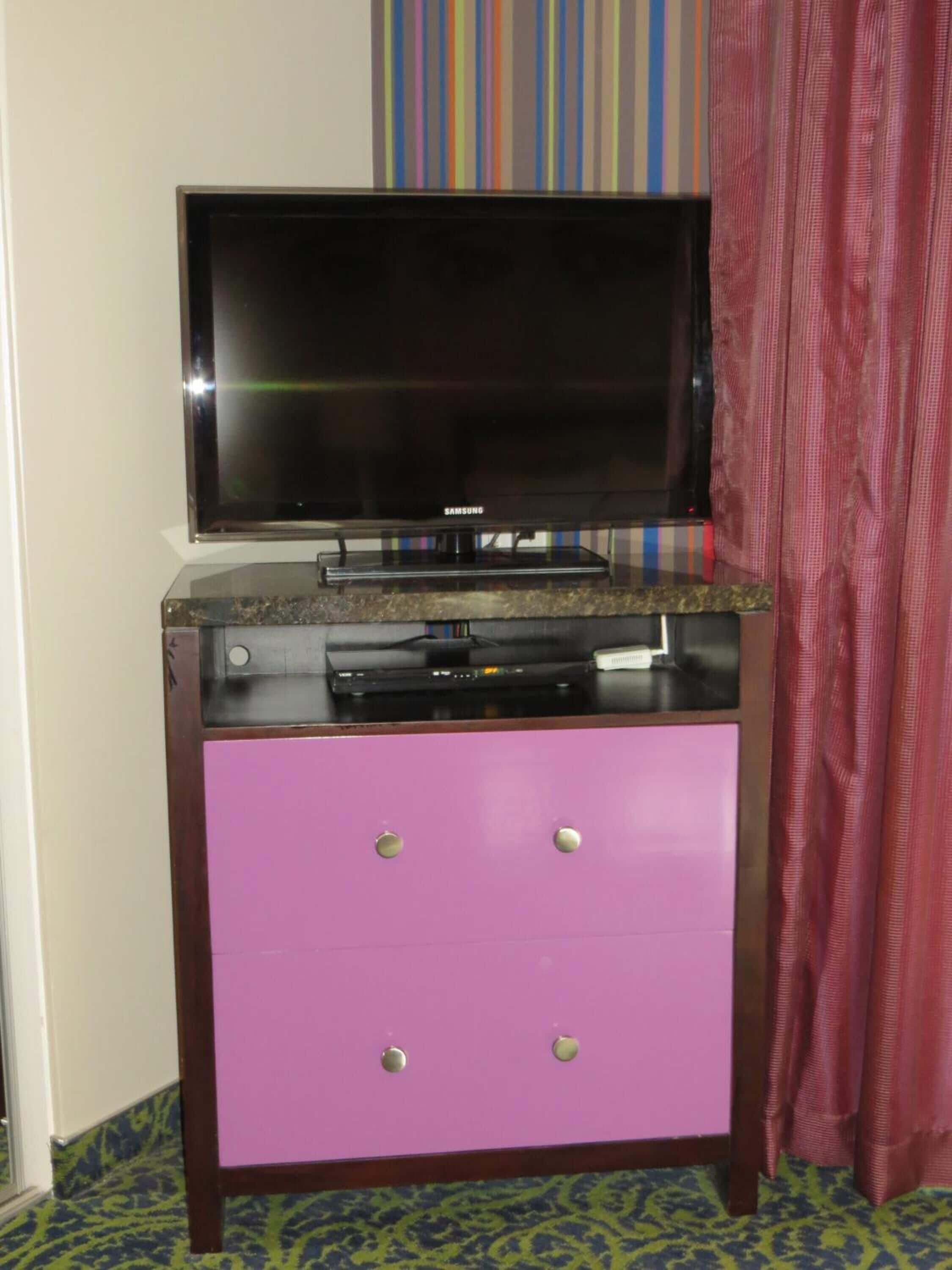 A television on a wooden cabinet with a pink drawer.