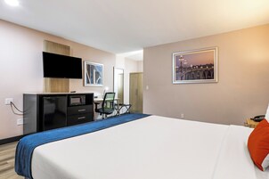 Habitación de hotel con cama, escritorio con computadora, televisor y un cuadro de un puente.