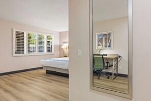A hotel room with a bed, a desk with a chair, a lamp, and a window with blinds.