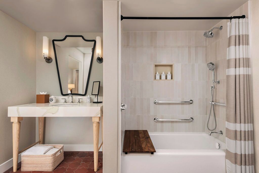 A bathroom with a white vanity, a mirror, a shower with a grab bar, and a wooden shelf.