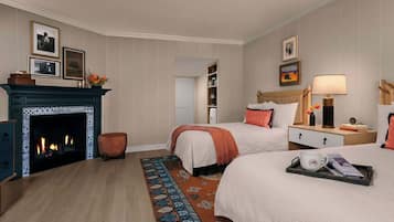 Une chambre d’hôtel avec deux lits, une cheminée, une table de chevet, une lampe et un plateau avec une tasse et un magazine.
