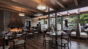 A restaurant with wooden flooring, brick walls, and hanging pendant lights. Tables are set with wine glasses and plates.