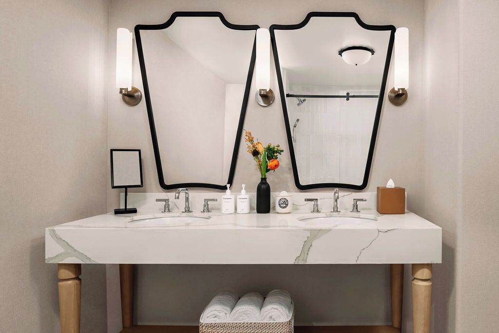 Casa de banho com dois espelhos, lavatório de mármore branco e toalheiro com toalhas.