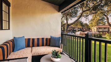 A covered outdoor seating area with a sofa and a round table, overlooking a well-maintained lawn and neighboring buildings.